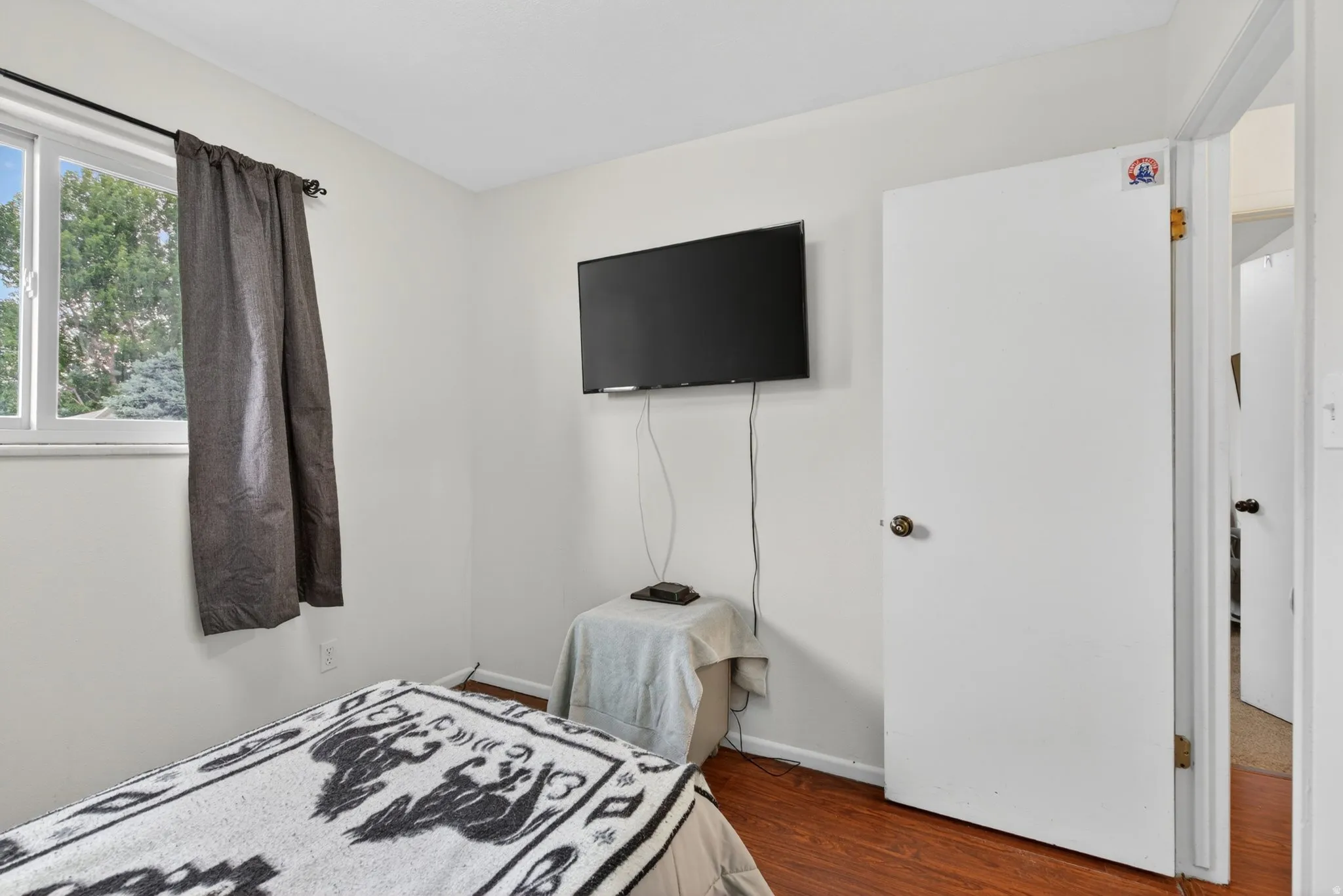 Bedroom featuring wood-finish flooring, a white-framed window, and neutral wall paint