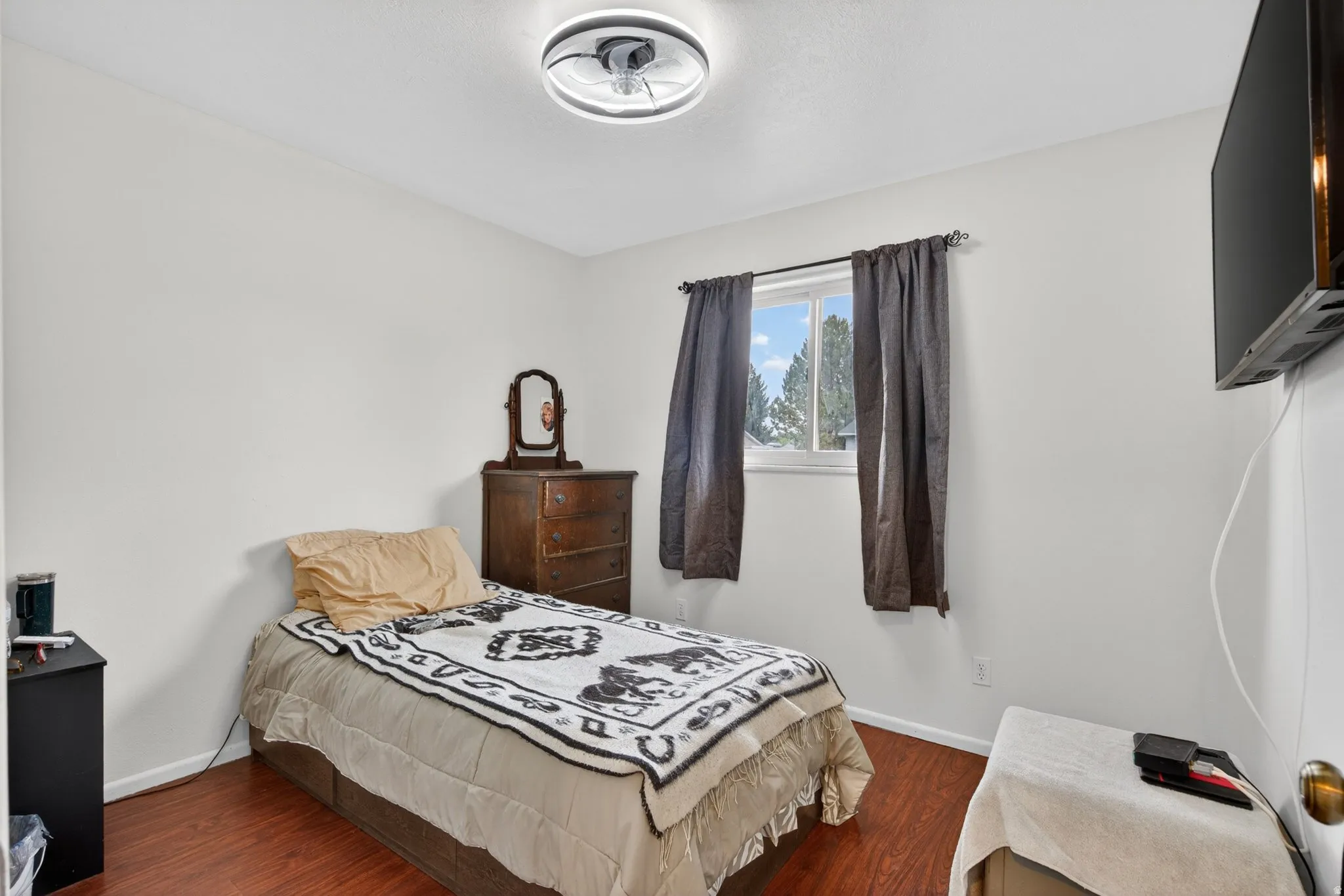 Room featuring wood-finish flooring, a window with dark curtain rods, white walls, and a contemporary ceiling light fixture