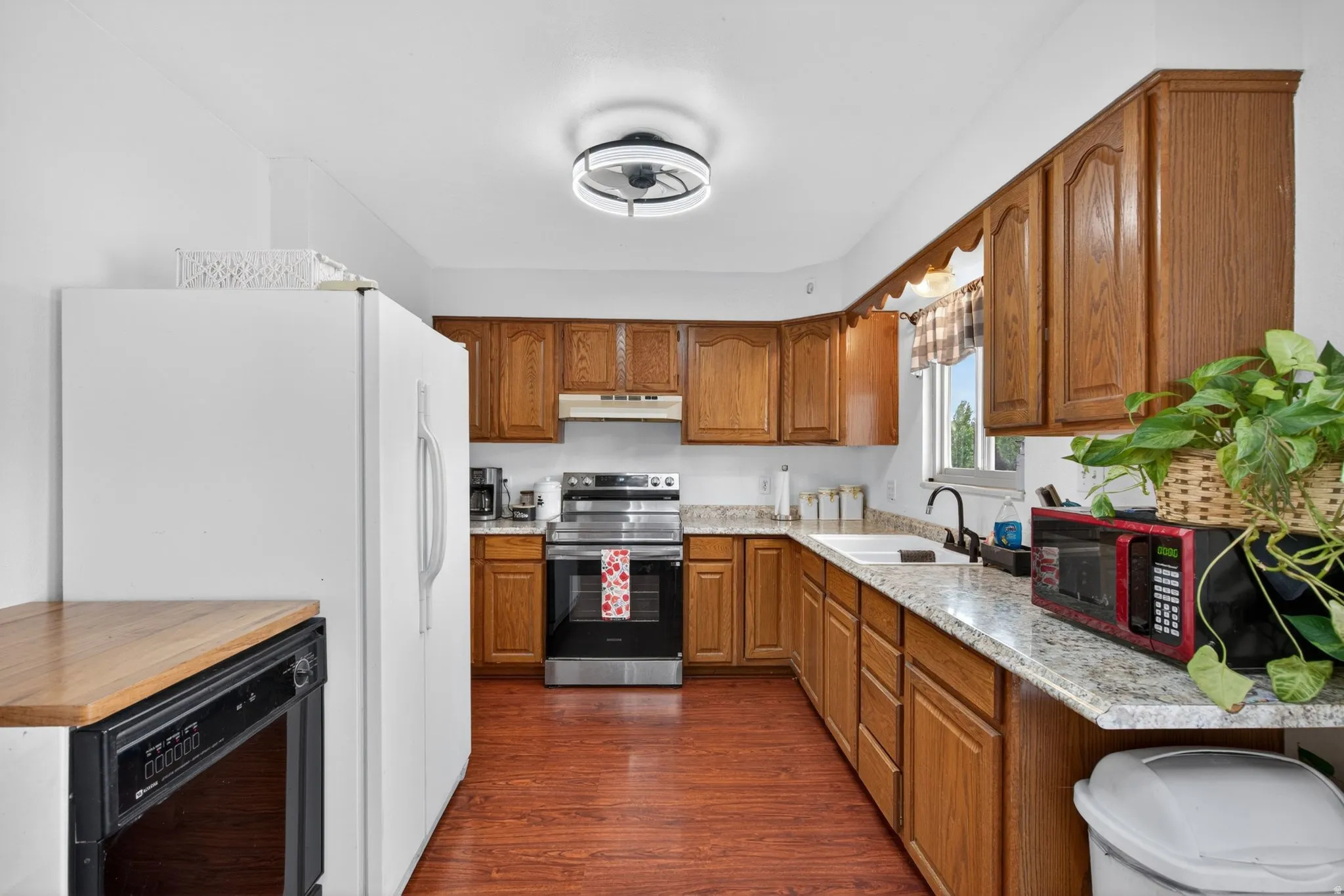 Kitchen featuring wood-finish flooring, oak cabinetry, granite-style countertops, a stainless steel range, and a white refrigerator