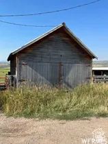 Gable-roof structure featuring vertical wood siding, double barn doors with metal hardware, and a gravel foreground