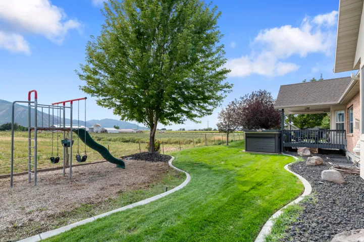Expansive backyard featuring a manicured lawn, landscaping with decorative rock and boulders, a covered patio, and a dedicated play area with a swing set