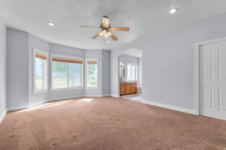 Spacious room featuring light brown carpeting, a bay window with multiple panes, a ceiling fan with integrated lighting, and recessed ceiling lights