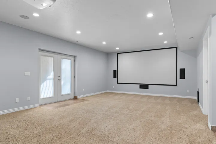 Spacious entertainment room featuring a large projection screen, built-in speakers, recessed lighting, and soft carpeting
