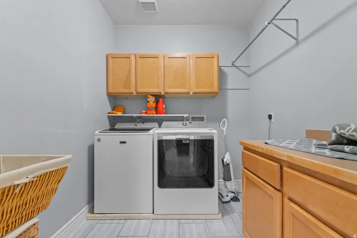 Dedicated laundry room featuring light wood-finish cabinetry, a built-in folding counter, a wall-mounted drying rack, and tile flooring
