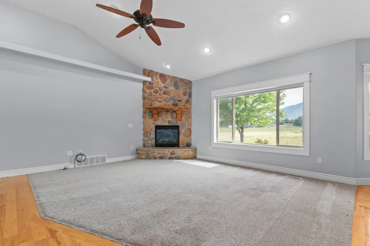 Spacious living area featuring a stone-clad fireplace with wood mantel, vaulted ceilings, and a ceiling fan