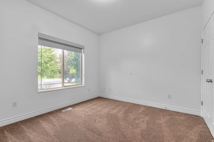 Bright room featuring a large window with roller shades, neutral carpeting, white baseboards, and a paneled door