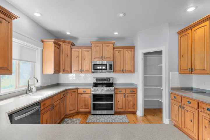 Kitchen featuring wood cabinetry, light countertops, subway tile backsplash, stainless steel appliances, and wood-finish flooring