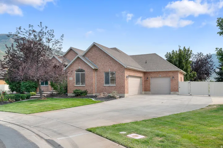 Brick exterior with multiple gables, arched window, attached two-car garage, expansive concrete driveway, and white privacy fence