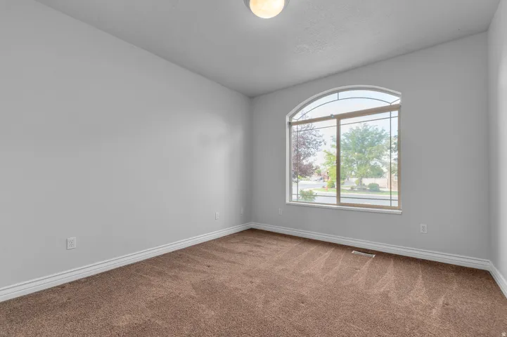 Room featuring an arched window, light gray walls, brown carpet flooring, and white baseboards