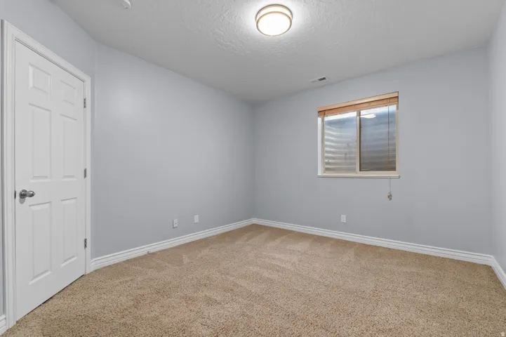 Carpeted room featuring a white paneled door, light gray walls, white baseboards, and a window with wood-finish blinds