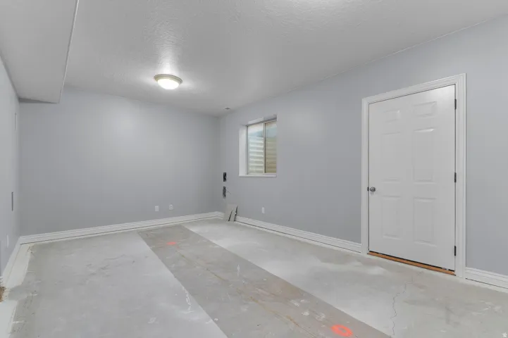 Spacious room with light gray walls, a window featuring horizontal blinds, and a white paneled door with brushed nickel hardware