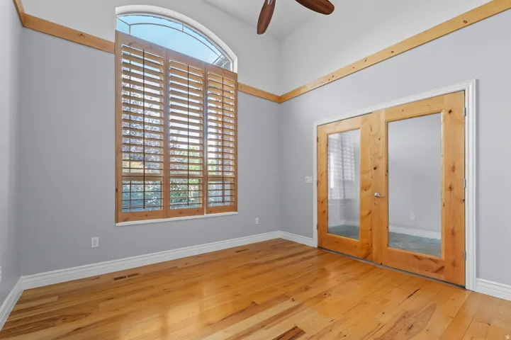 Vaulted ceiling room featuring tall arched windows with plantation shutters, wood-finish flooring, natural wood trim accents, and French doors with clear glass panels