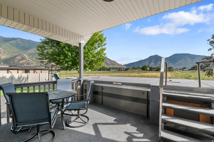 Covered patio space featuring a hot tub, mountain backdrop, and expansive field