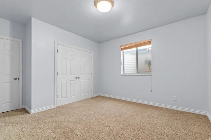 Carpeted room featuring a double-door closet, a single window with blinds, and white trim