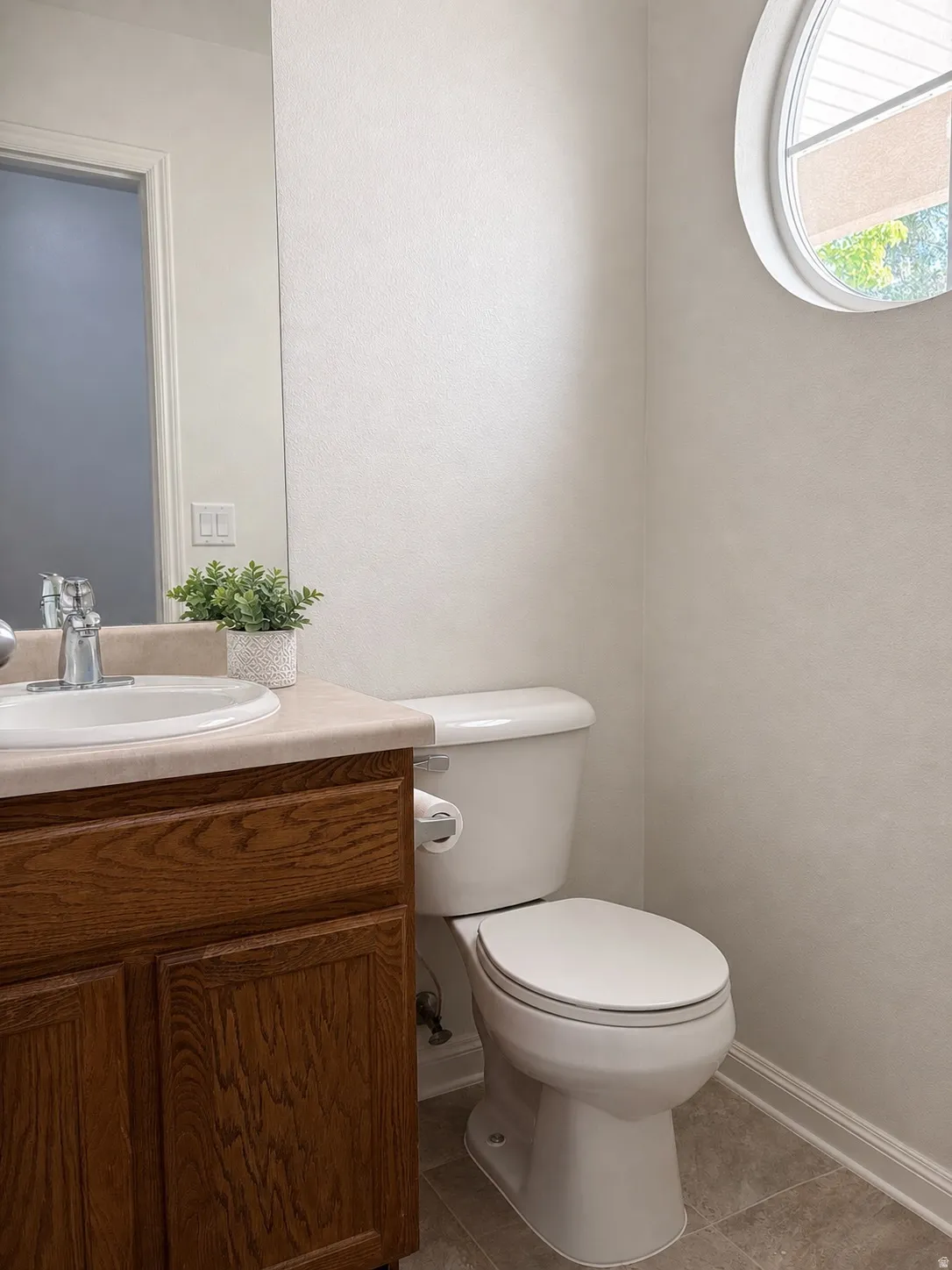 Bathroom featuring a round architectural window, wood-finish vanity with an integrated sink, and tile flooring