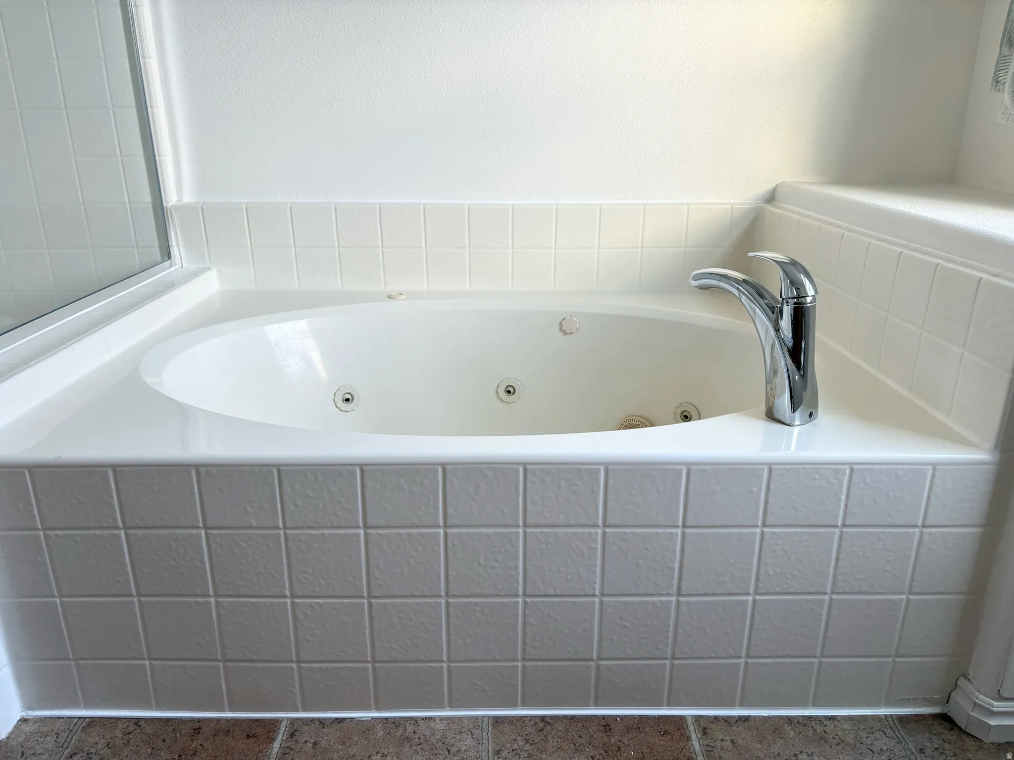 White jetted bathtub with a chrome faucet, surrounded by square white tile detailing and a tiled floor