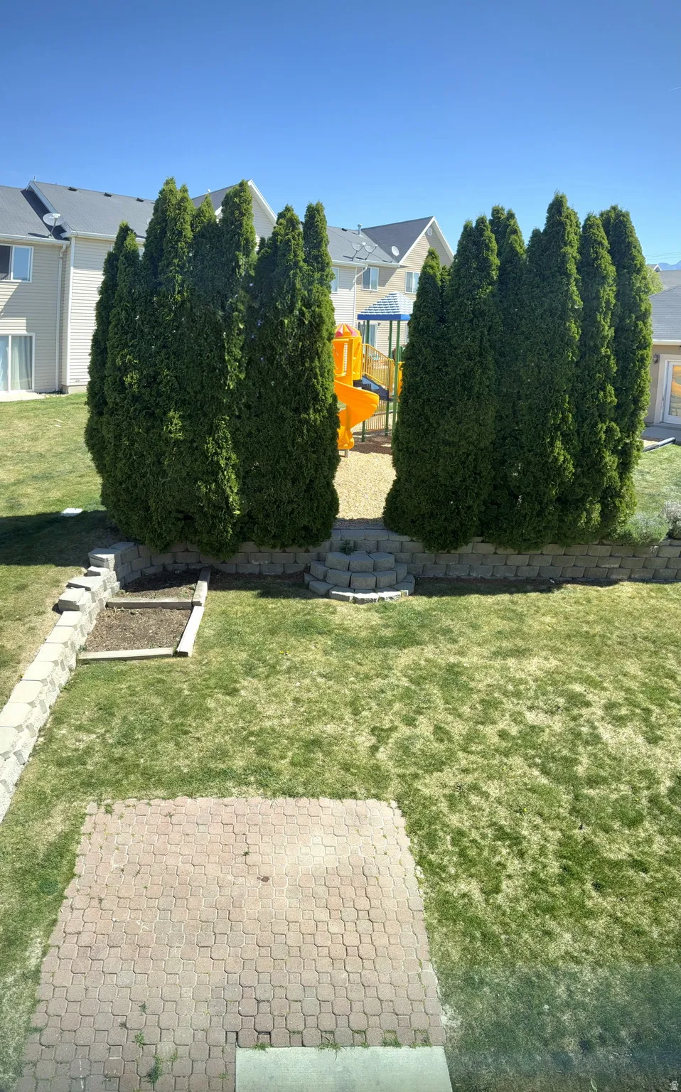 Expansive backyard featuring a paver patio, stone retaining walls, and a dedicated garden bed