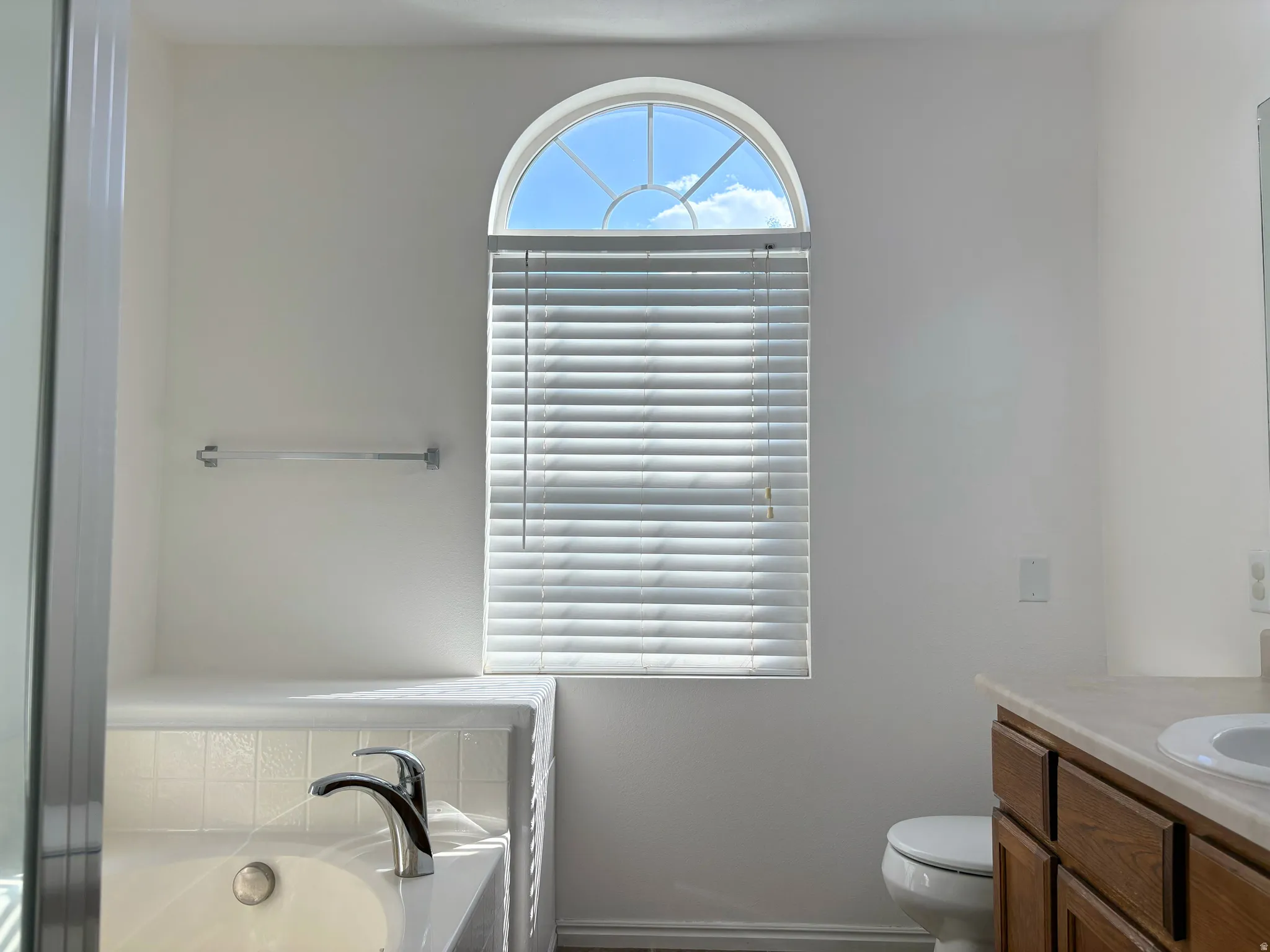 Built-in soaking tub with chrome faucet, featuring a tiled surround and an arched window with blinds
