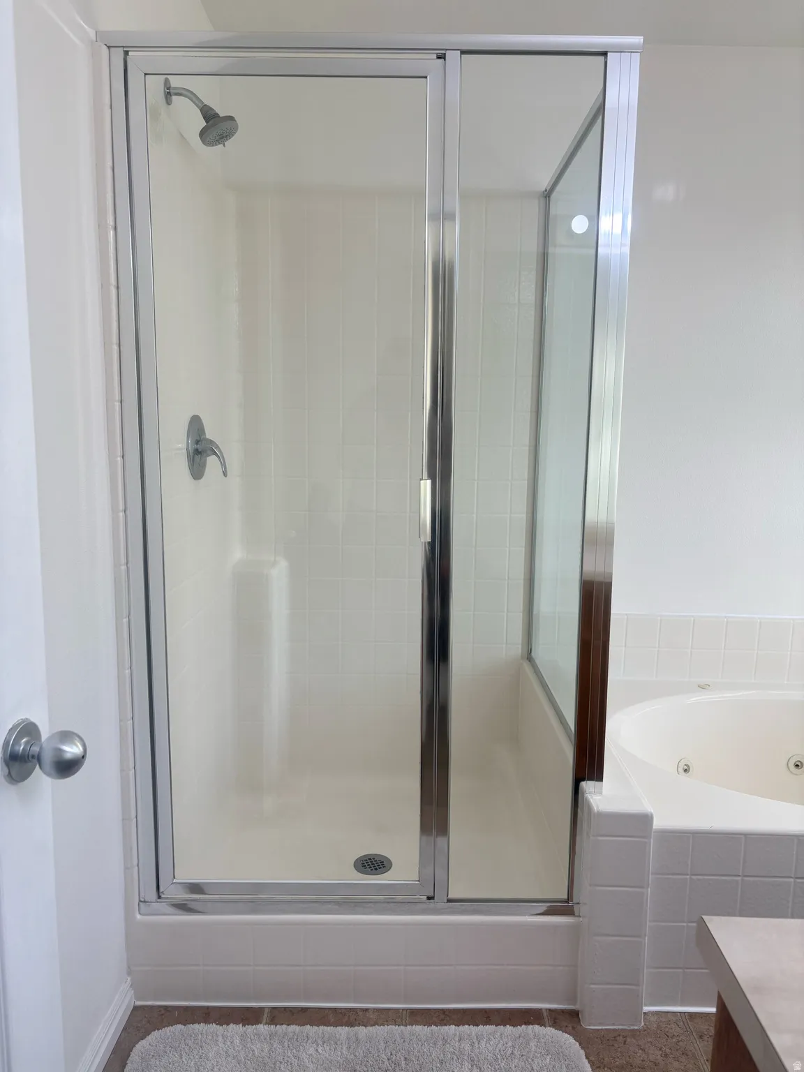 Glass-enclosed shower with chrome fixtures and white tiled walls