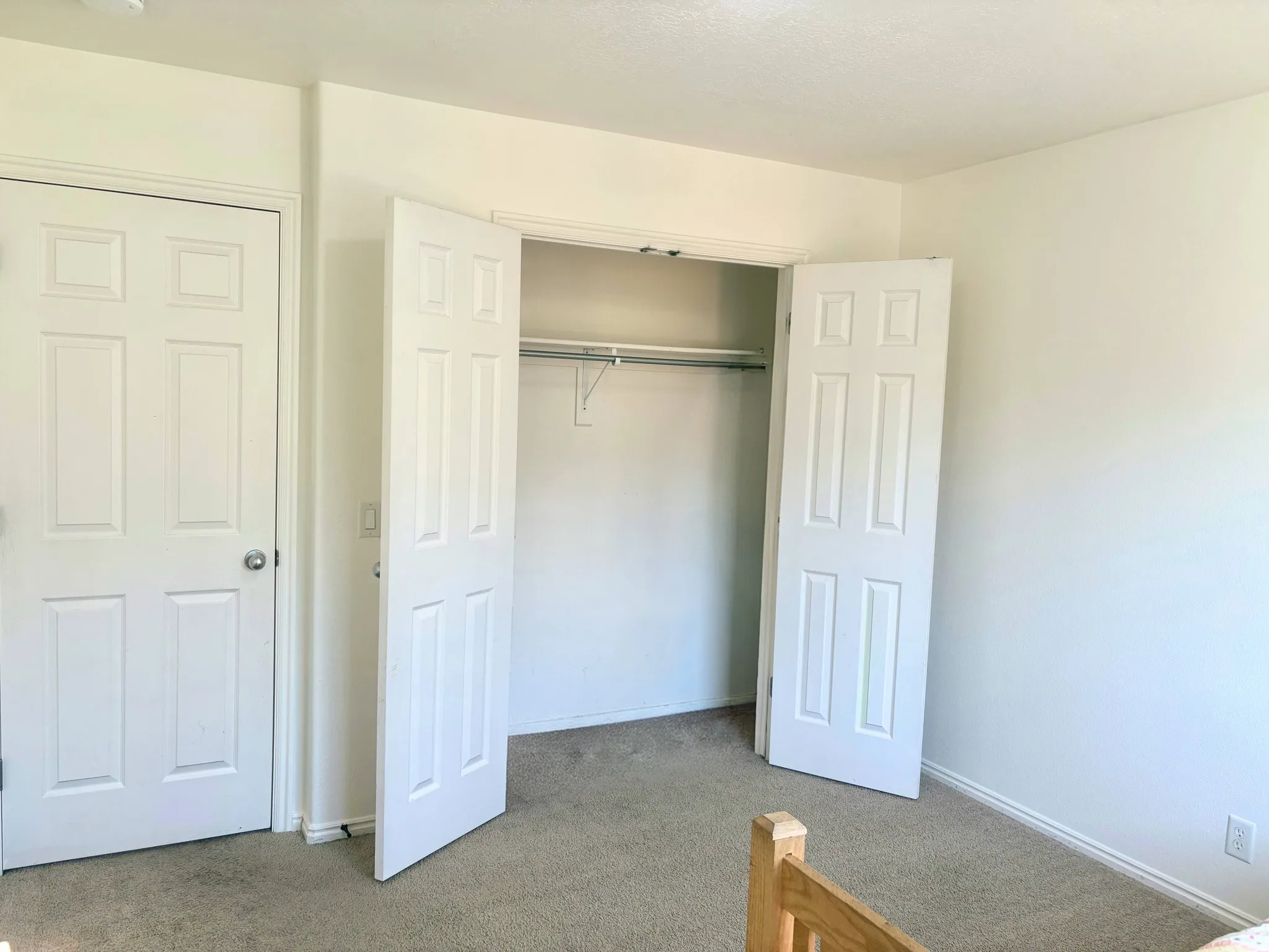 Room featuring a white interior door with a paneled design, a closet with bifold paneled doors, and light-toned carpeting