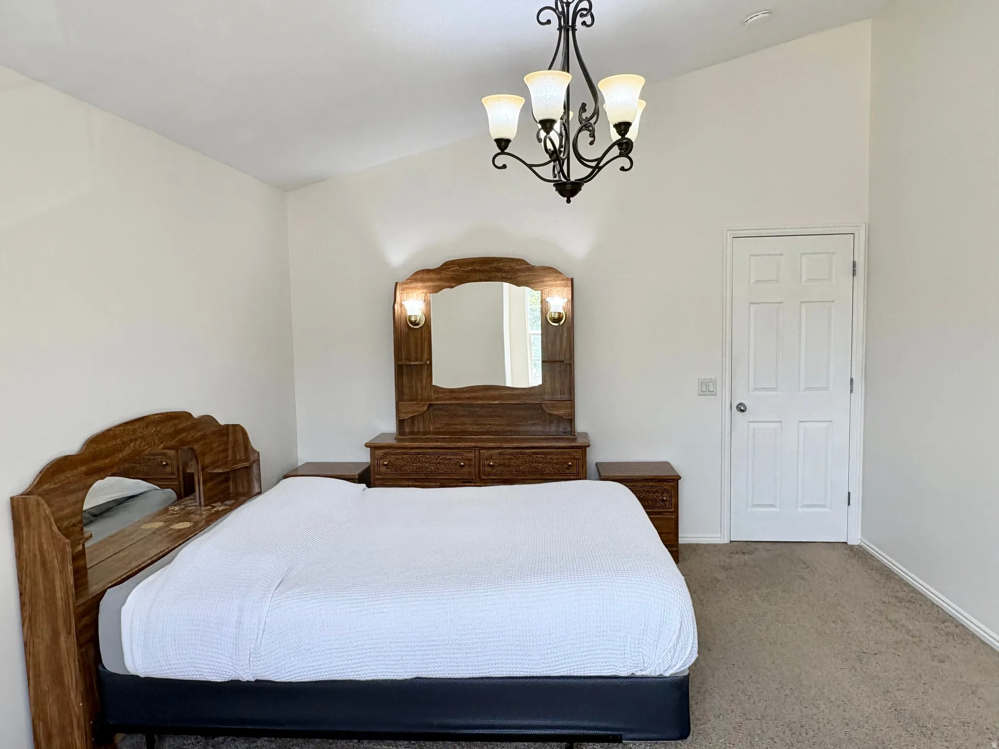 Vaulted ceiling bedroom featuring a five-light chandelier, neutral carpeting, and a white paneled door