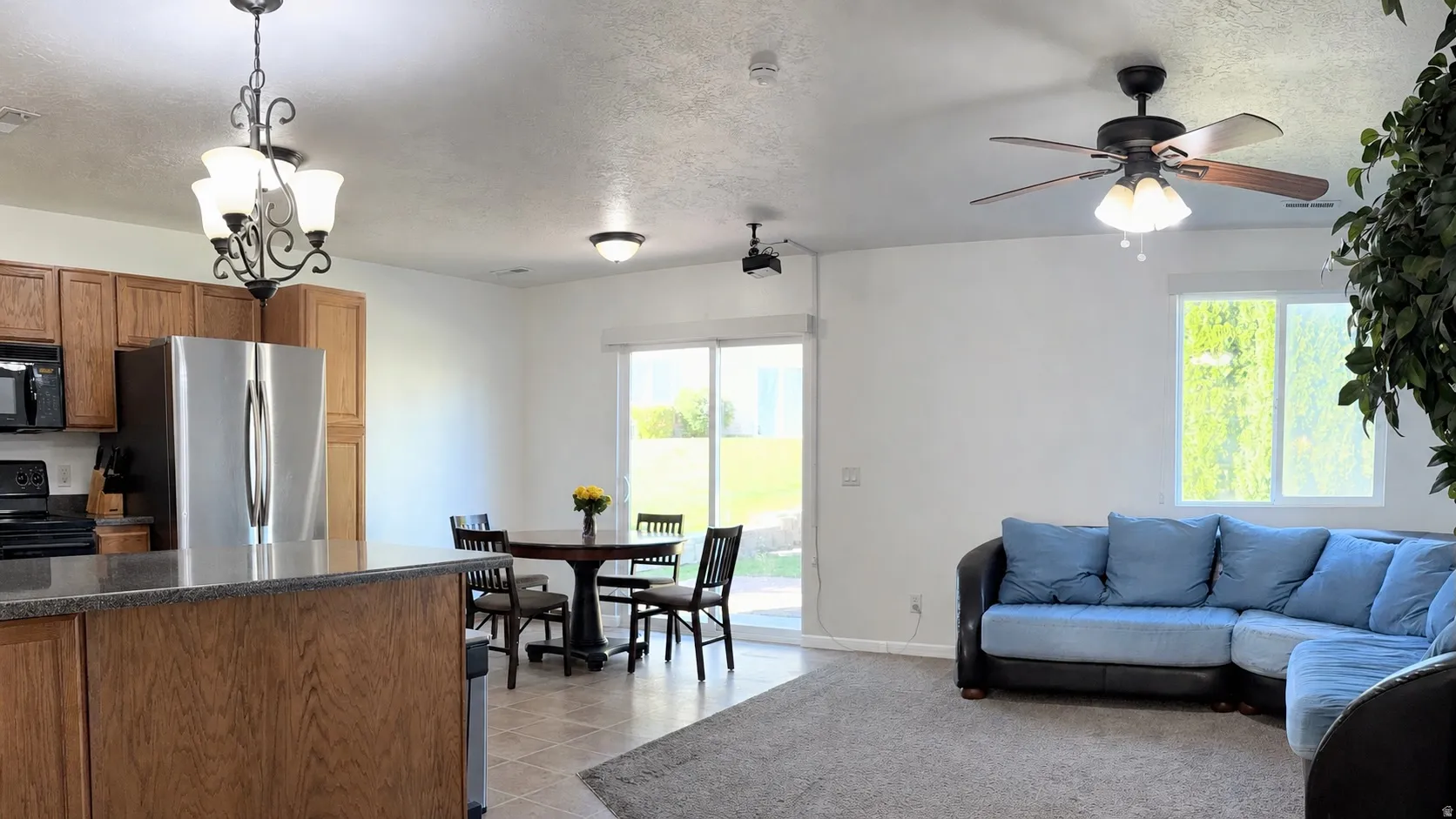 Open-concept living space featuring a kitchen with wood cabinetry and stainless steel appliances, a dining area with a sliding glass door, and a living area with a ceiling fan