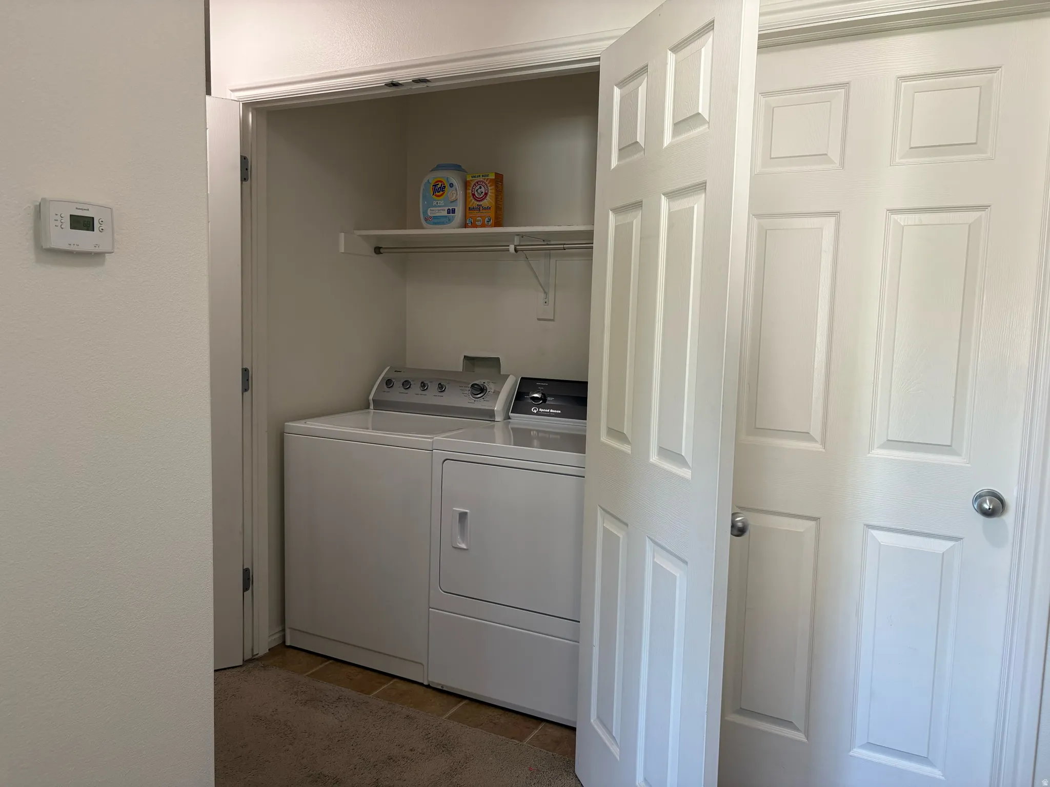 Laundry closet featuring a built-in shelf, white paneled bifold doors, and a tile floor
