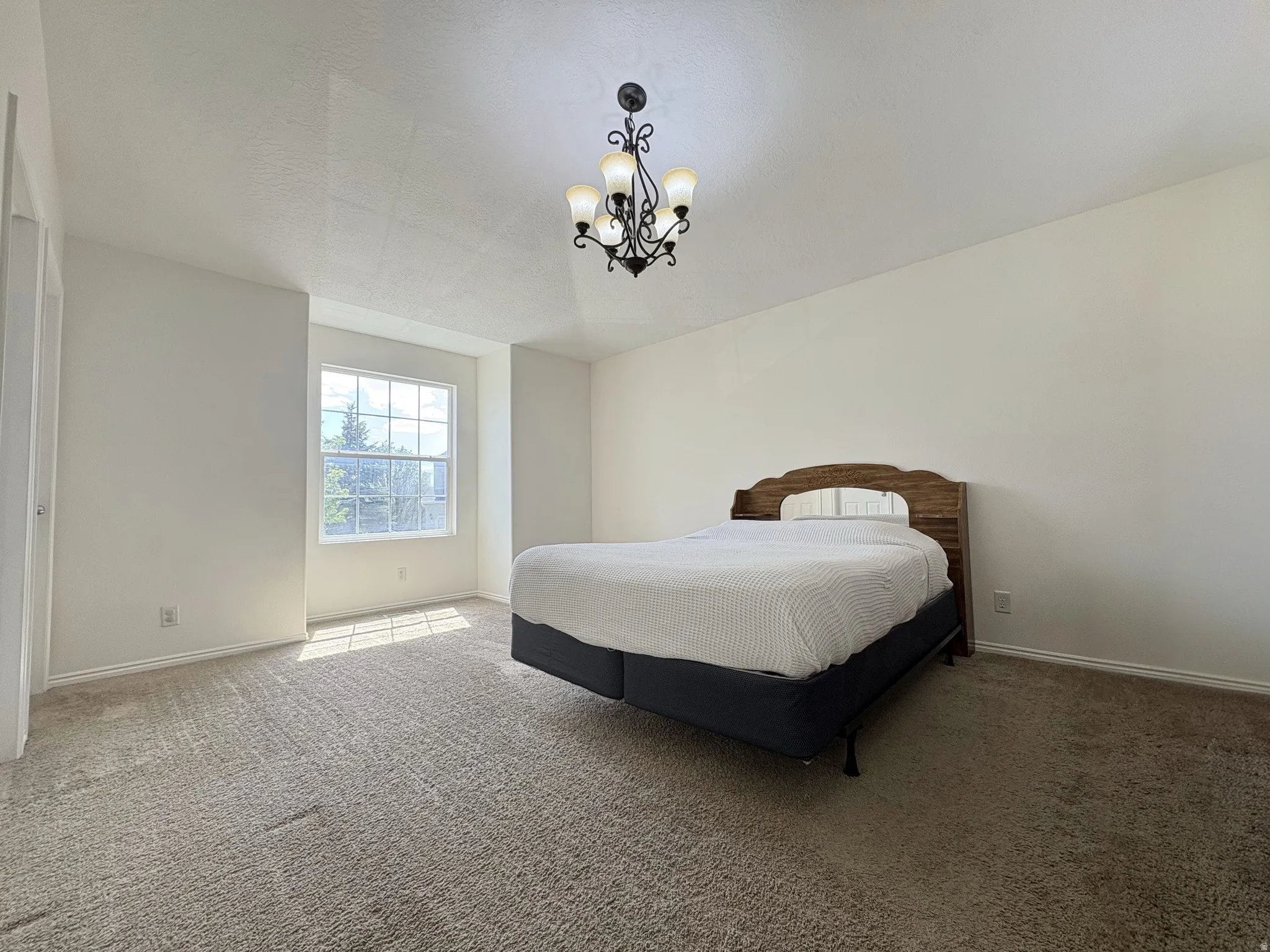 Spacious room featuring neutral carpeting, a multi-pane window, and a decorative chandelier