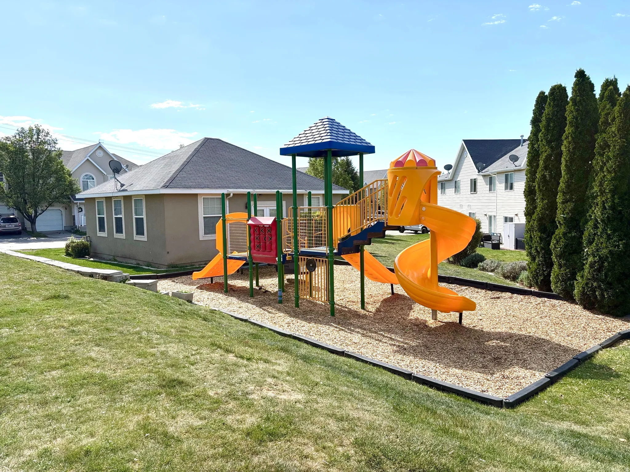 Outdoor playground structure with multiple slides and climbing elements, set on a wood chip base with black border