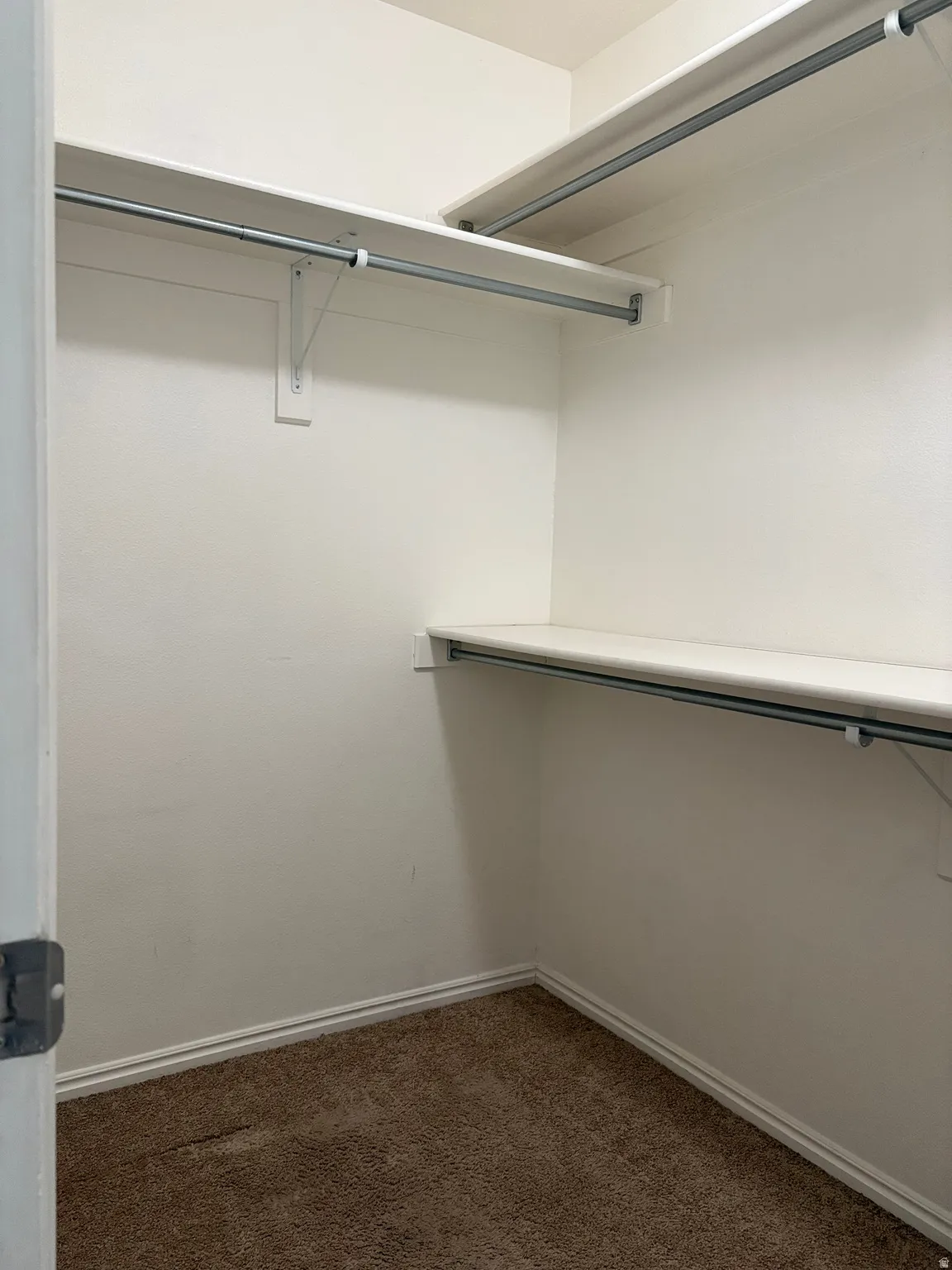 Walk-in closet featuring white walls, white shelving, and metal hanging rods