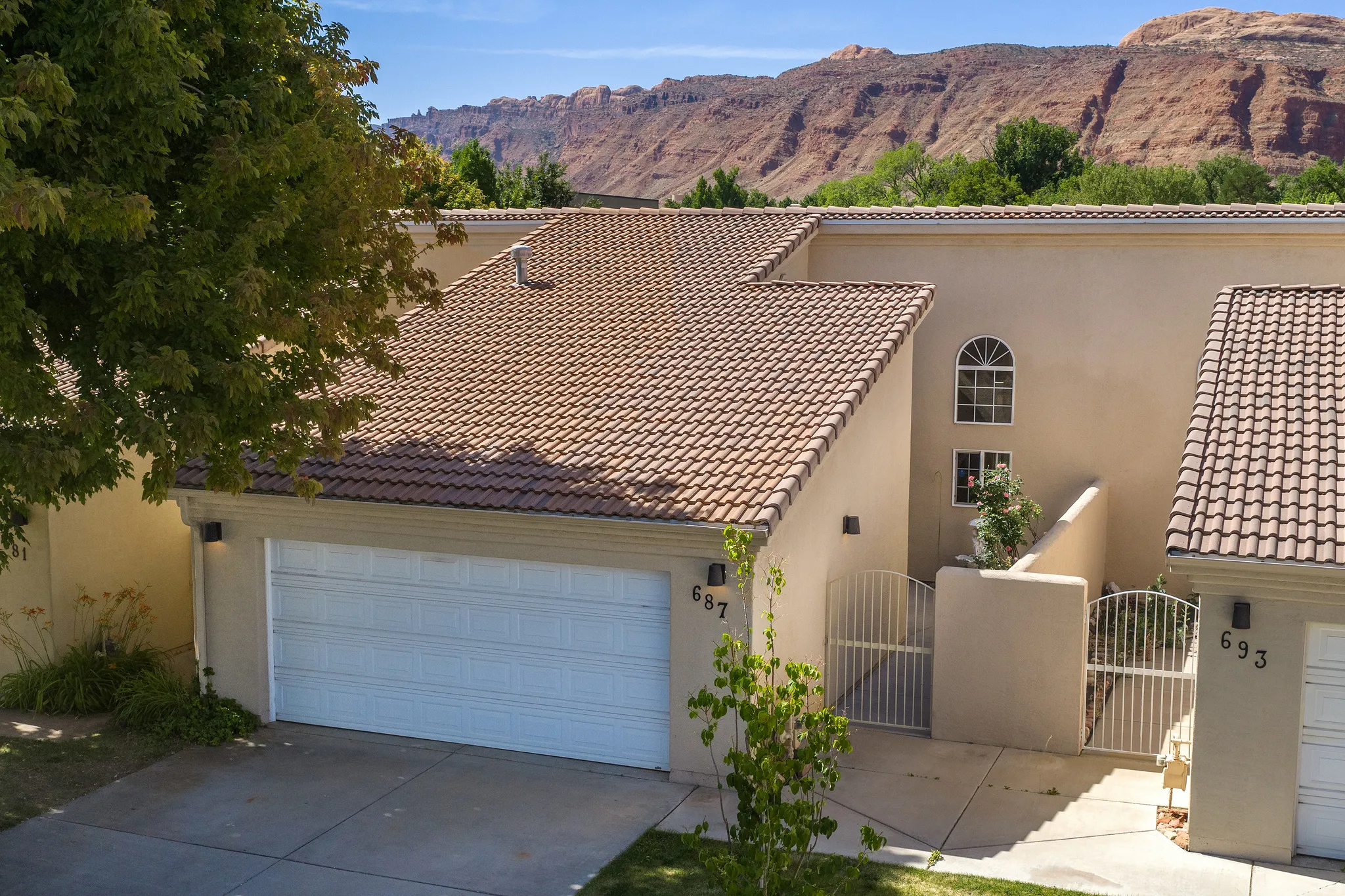 Stucco exterior with a tiled roof, featuring an attached garage, a gated courtyard entrance, and an arched window