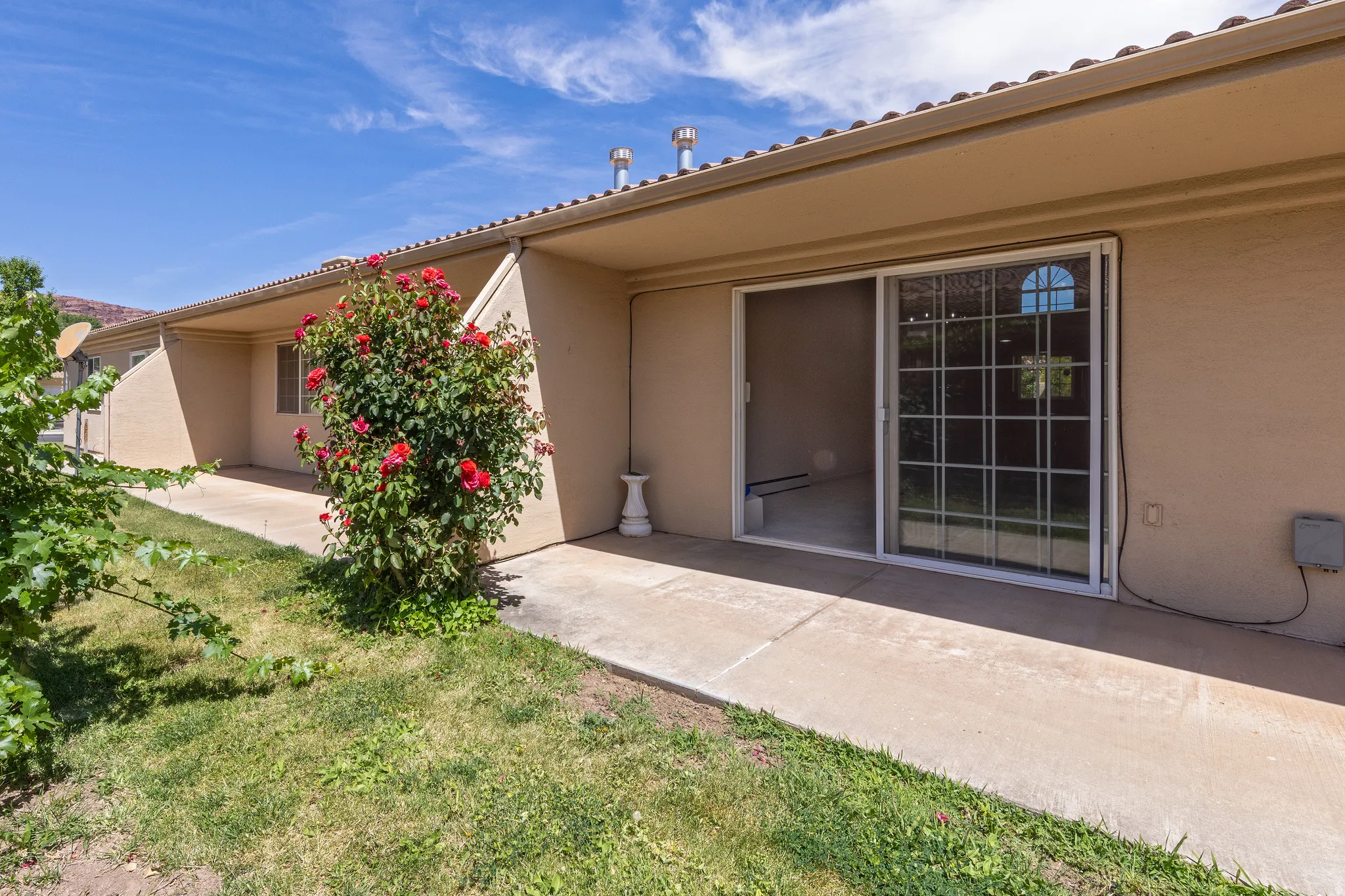 Patio area featuring a sliding glass door with grid panes, textured stucco exterior, and a flowering shrub