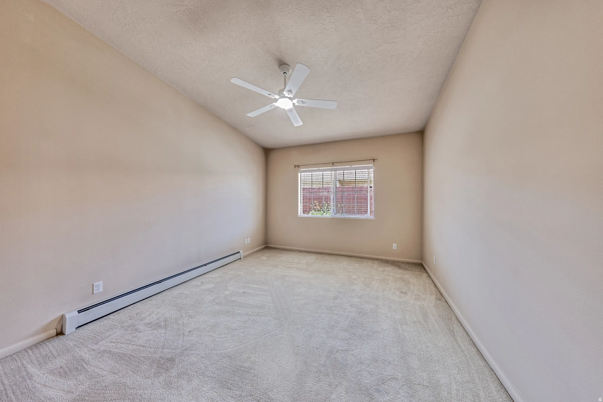Carpeted interior space featuring a window with blinds, a ceiling fan, and baseboard heating
