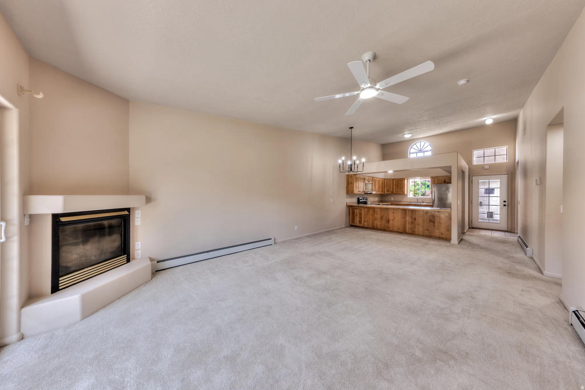 Spacious living area featuring a fireplace with a light-colored surround, vaulted ceilings, and light-toned carpet flooring