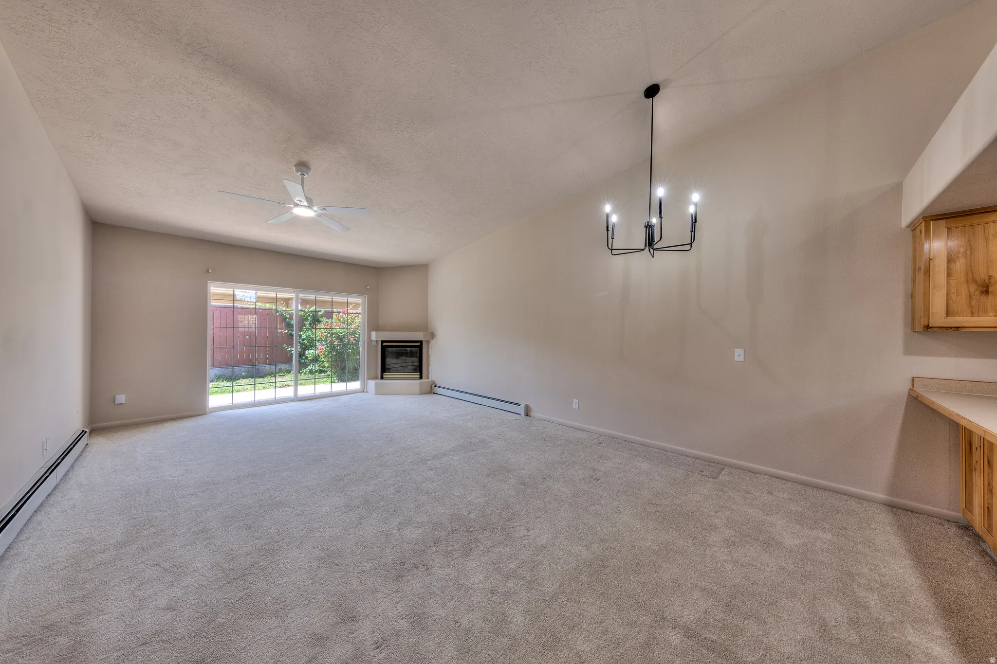 Spacious interior featuring vaulted ceilings, light-toned carpeting, a corner fireplace, and a sliding glass door to exterior