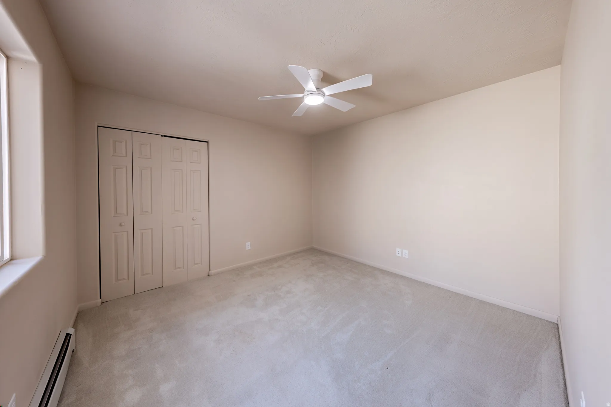 Carpeted room featuring a ceiling fan with integrated lighting, a window, baseboard heating, and a bi-fold closet with panel doors