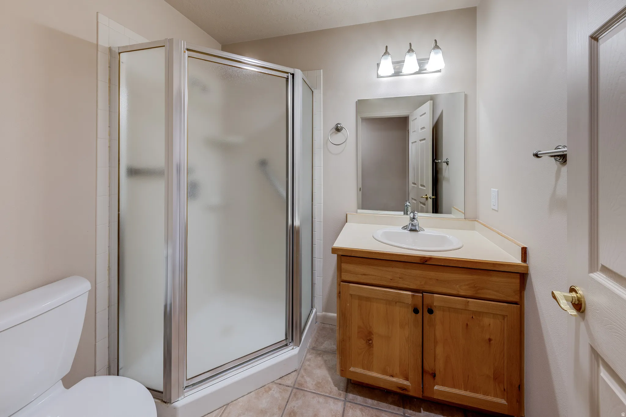 Bathroom featuring a corner shower with frosted glass enclosure, a single vanity with wood cabinetry and an integrated sink, a wall-mounted mirror, and tile flooring