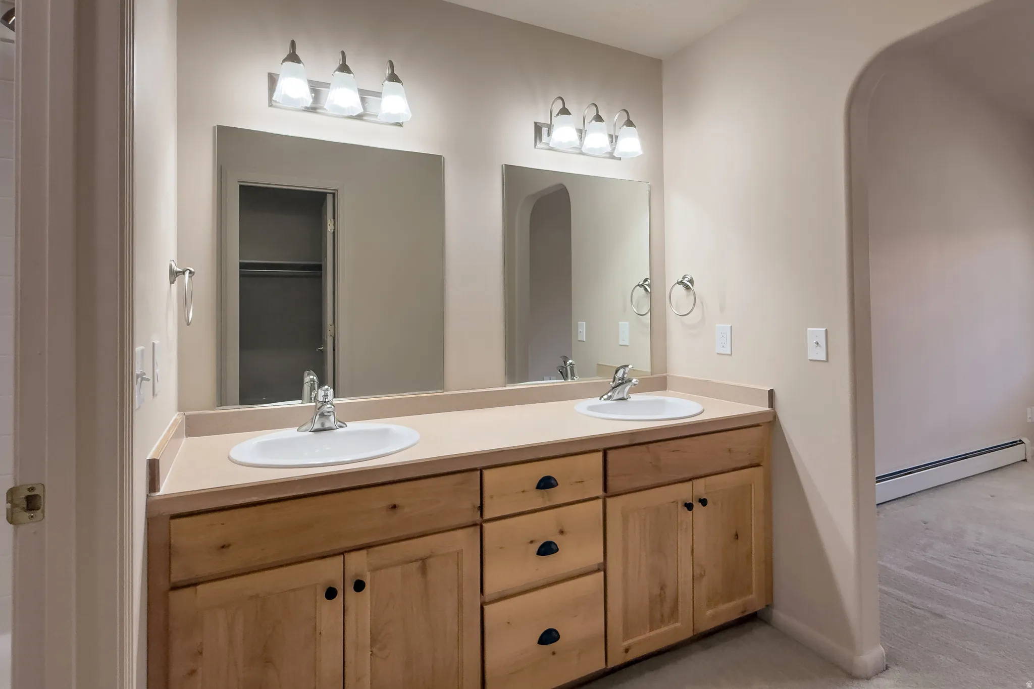 Dual vanity with light wood cabinetry, white oval sinks, and a light-toned countertop