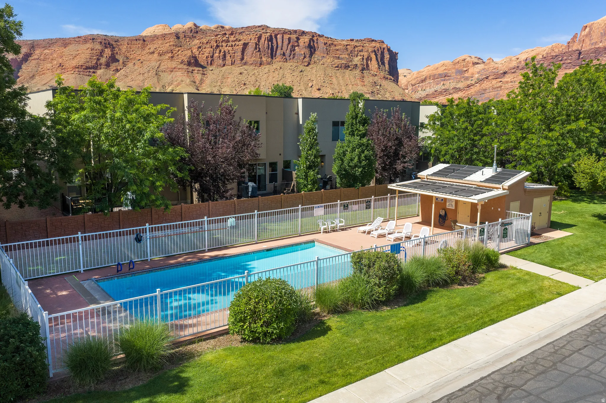 Community swimming pool with a surrounding fence, adjacent pool house, and a paved sun deck