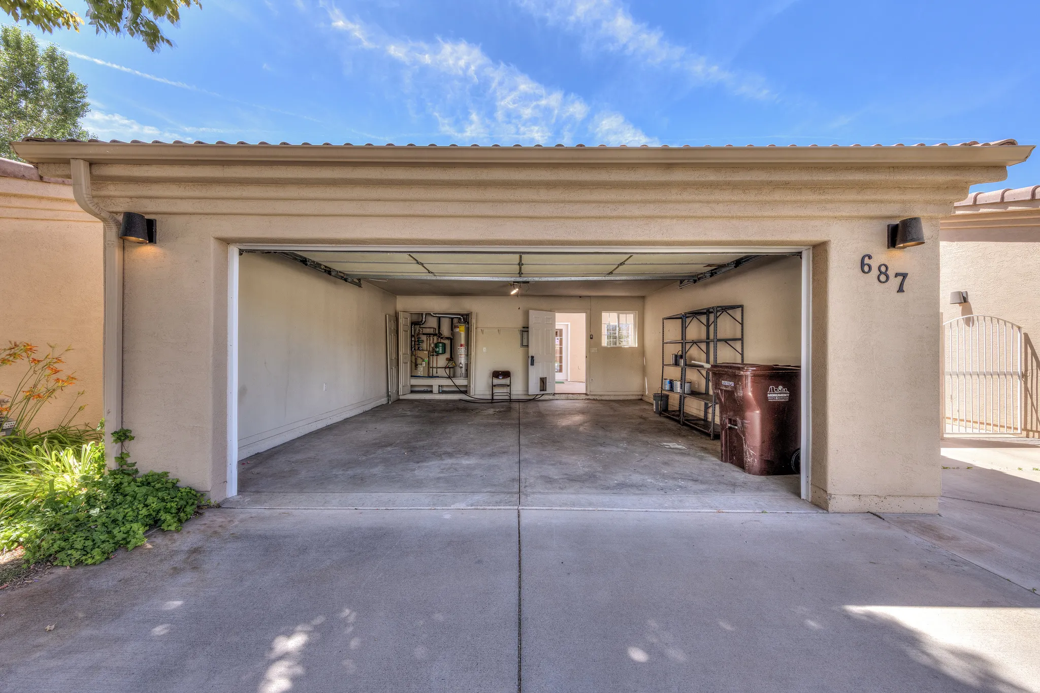 Attached two-car garage with concrete flooring, stucco exterior, wall-mounted exterior lighting, and a roll-up garage door