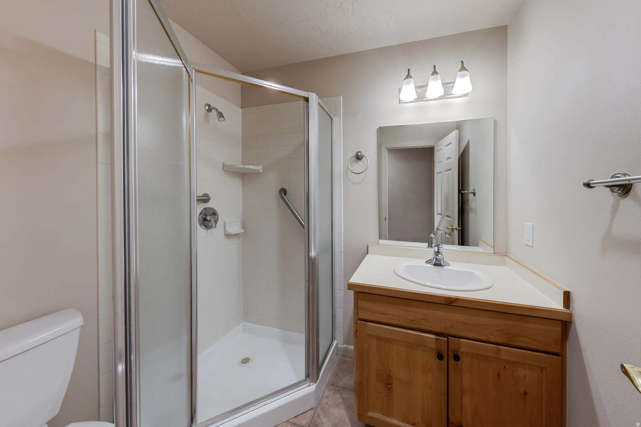 Enclosed shower with a grab bar and white base, complemented by a wood-finish vanity with an integrated sink and light-toned countertop