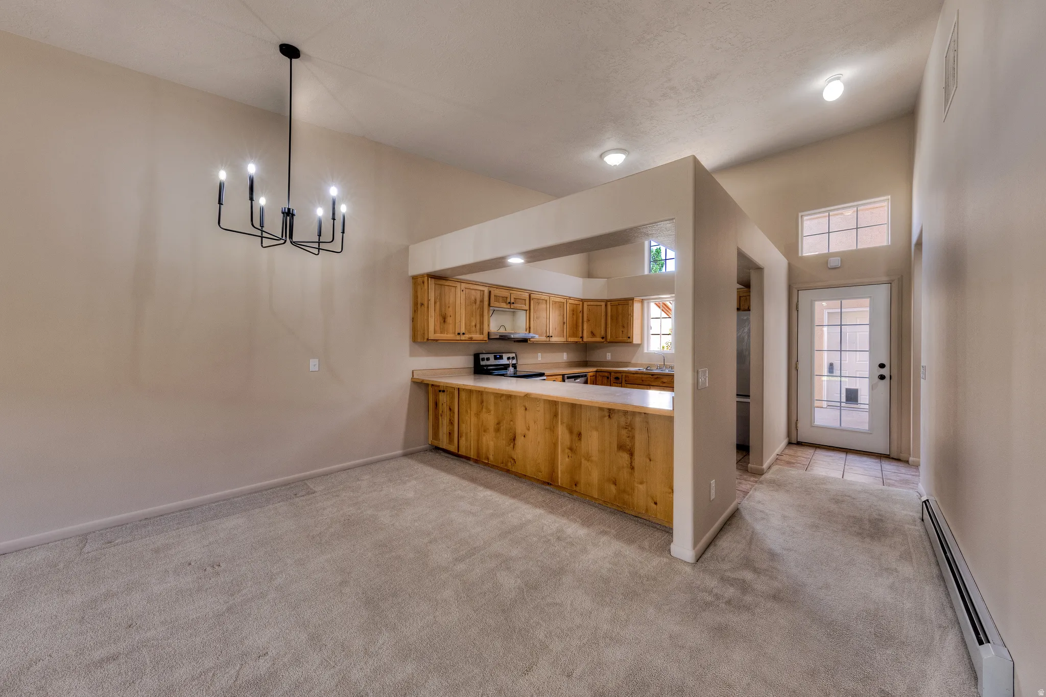 Carpeted dining area featuring a black metal chandelier, vaulted ceiling, and an open concept kitchen with wood cabinetry and light countertops