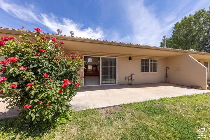 Rear exterior featuring a covered concrete patio, sliding glass door access to interiors, multiple windows, and a mature rose bush