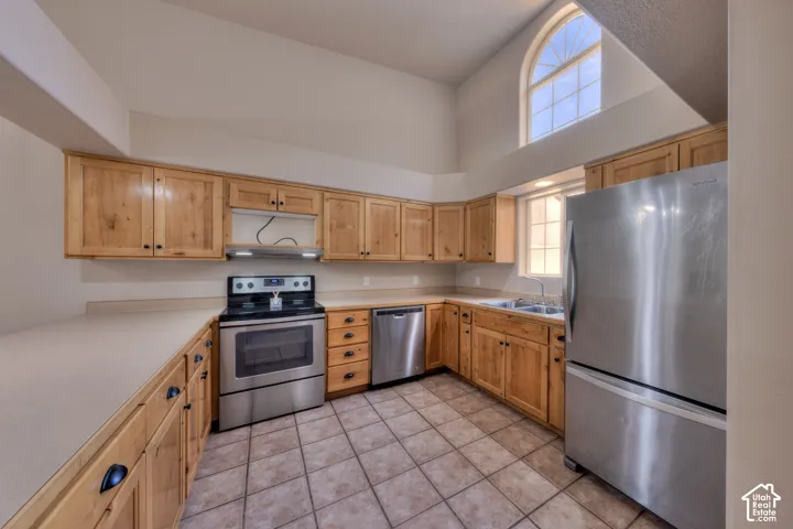 Kitchen featuring vaulted ceilings, an arched top window, light wood cabinetry, neutral countertops, and stainless-steel appliances