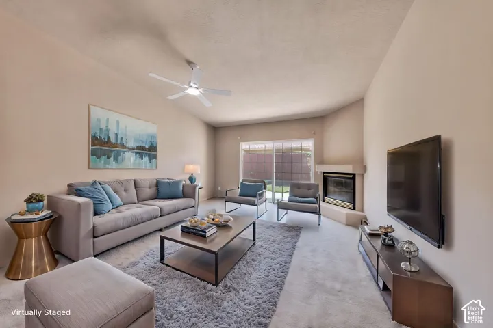 Living area featuring vaulted ceilings, a ceiling fan, plush carpet flooring, a corner fireplace, and sliding glass doors