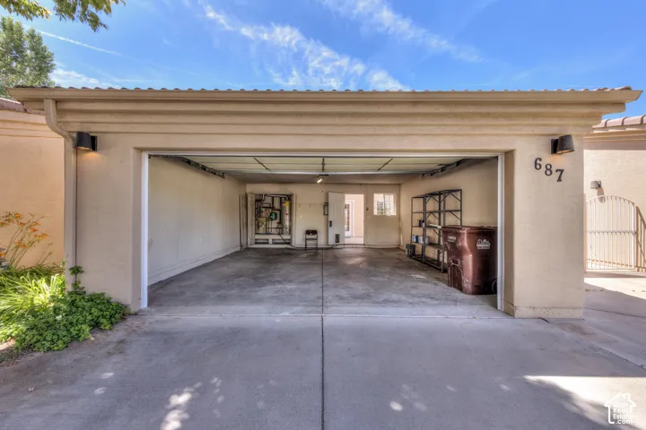 Attached two-car garage with concrete flooring, stucco exterior, wall-mounted exterior lighting, and a roll-up garage door