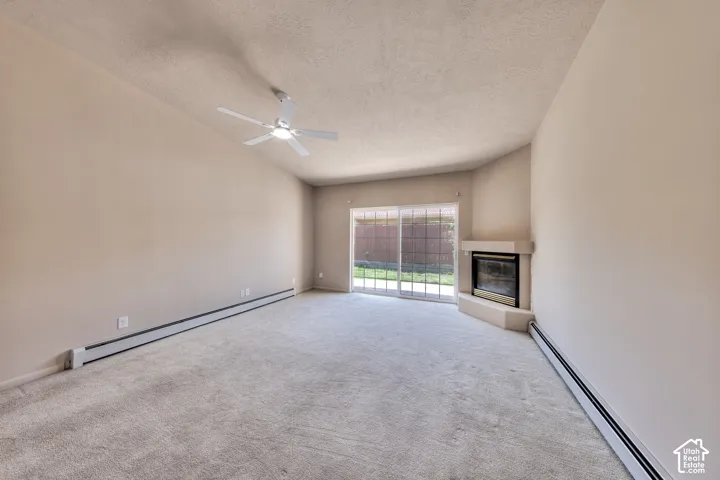 Carpeted living area featuring a corner fireplace with a light-toned surround, a ceiling fan, and sliding glass doors opening to a fenced outdoor area with grass