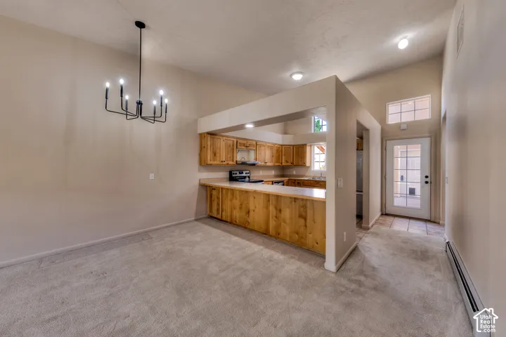 Carpeted dining area featuring a black metal chandelier, vaulted ceiling, and an open concept kitchen with wood cabinetry and light countertops