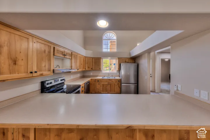 Kitchen featuring extensive wood cabinetry, light-toned countertops, stainless steel appliances, and a vaulted ceiling with an arched window