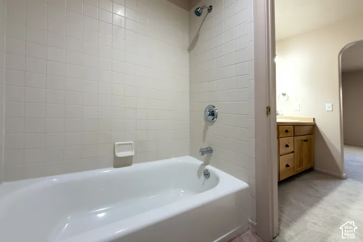 White subway tile surround with chrome fixtures, a classic white bathtub, a natural wood-finish vanity with cabinet storage and drawers, and an arched hallway opening